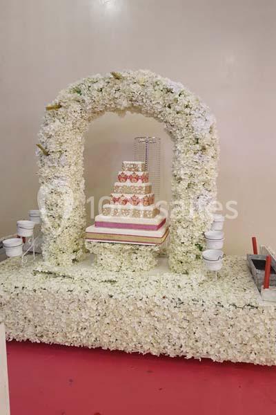 Arche florale blanche entourant un gâteau décoratif à plusieurs étages, posée sur une base ornée de fleurs.