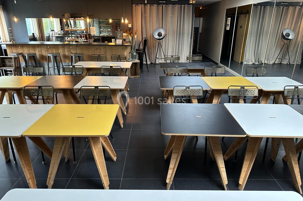 Salle moderne avec tables colorées en bois, chaises métalliques, grand miroir et comptoir en arrière-plan.