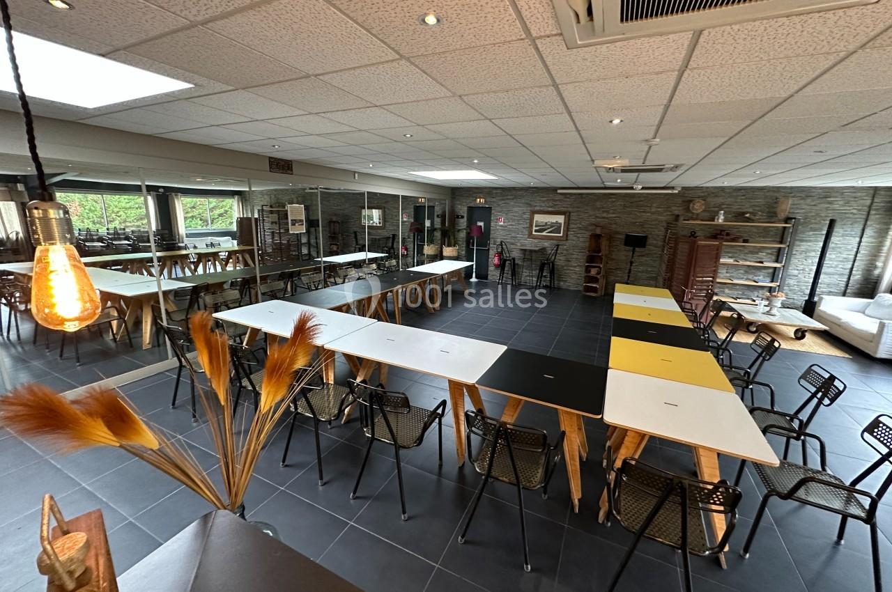 Salle de réunion moderne avec tables disposées en U, chaises noires, éclairage chaleureux et grandes baies vitrées.