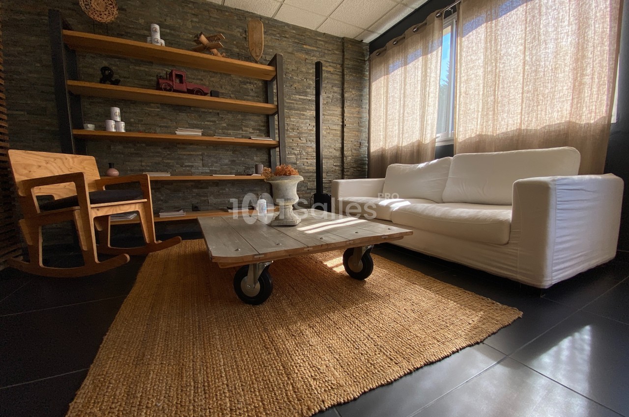Salon lumineux avec canapé blanc, table basse en bois sur roulettes, fauteuil à bascule et étagères en fond.