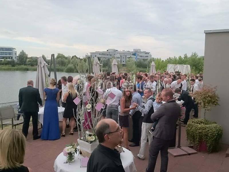 Groupe de personnes rassemblées sur une terrasse près d'un plan d'eau, lors d'un événement en plein air.