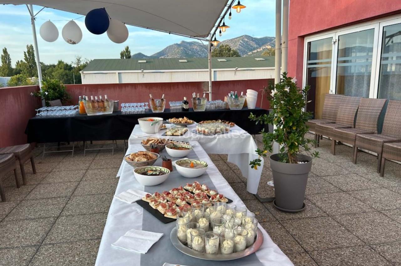 Buffet dressé en extérieur sous une tente, avec divers plats et boissons, sur une terrasse avec vue sur des montagnes.