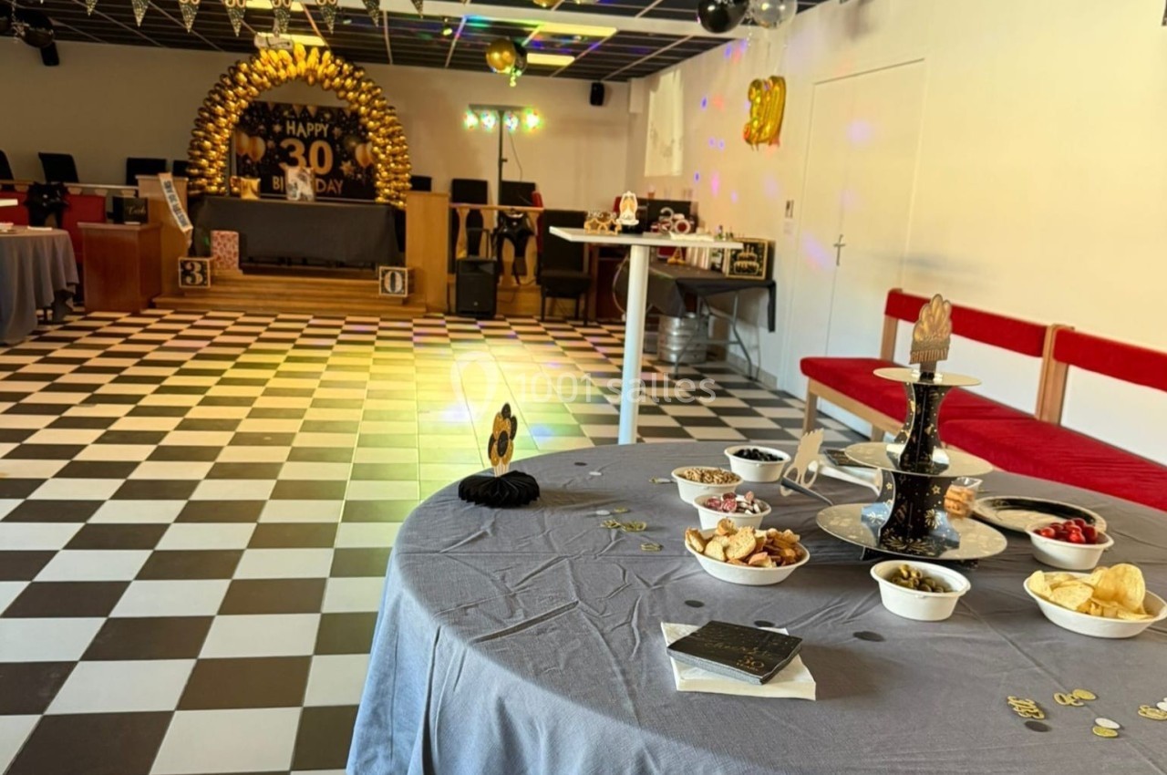 Salle décorée pour une fête d'anniversaire avec tables garnies, décorations dorées et sol en damier noir et blanc.