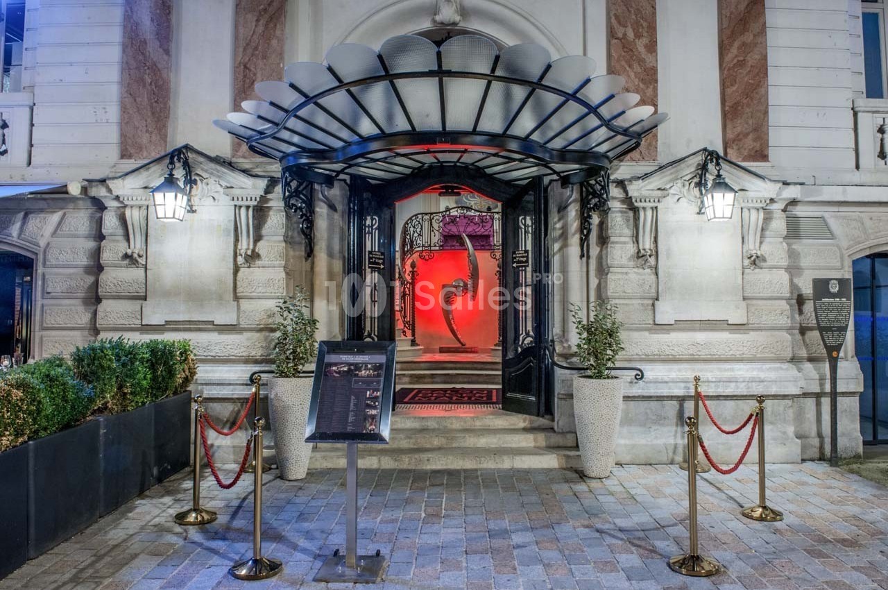 Entrée d'un bâtiment élégant avec porte ouverte, tapis rouge, éclairage rouge et cordons de sécurité.