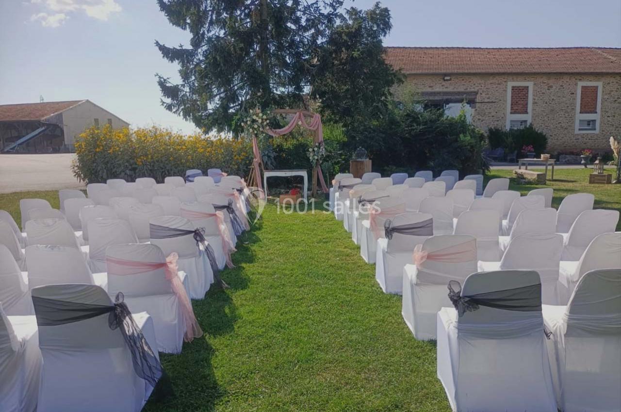 Chaises blanches décorées en rangées face à une arche ornée de tissu rose, installées sur une pelouse en extérieur.