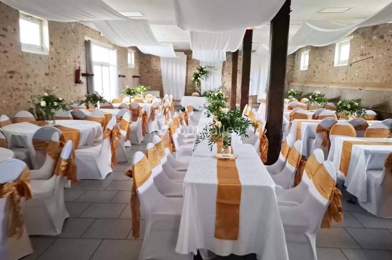 Salle de réception décorée avec des tables dressées, nappes blanches, chemins de table orange et compositions florales.