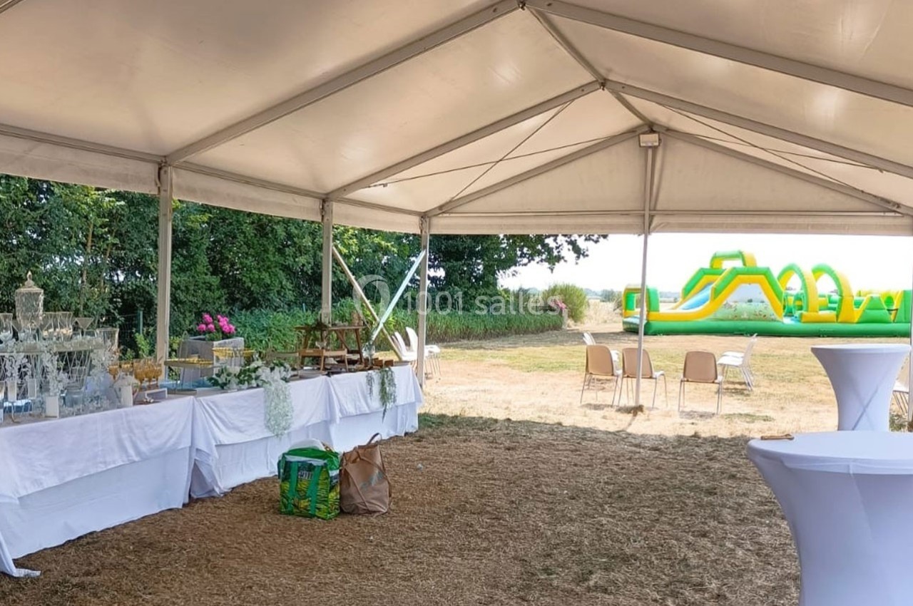 Intérieur d'une tente avec tables dressées, vue sur un espace extérieur avec structure gonflable colorée.