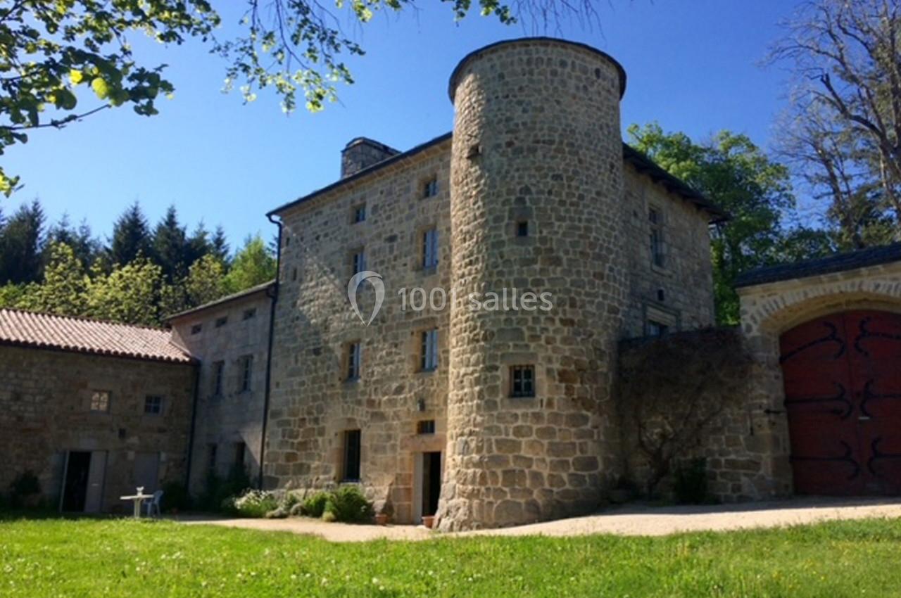 Bâtisse en pierre avec une tour ronde, entourée de verdure et éclairée par un ciel bleu dégagé.
