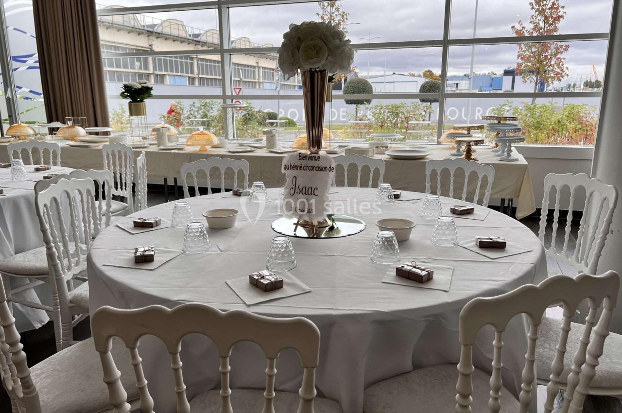 Table de réception décorée avec nappes blanches, chaises assorties, centre de table floral et vaisselle disposée.