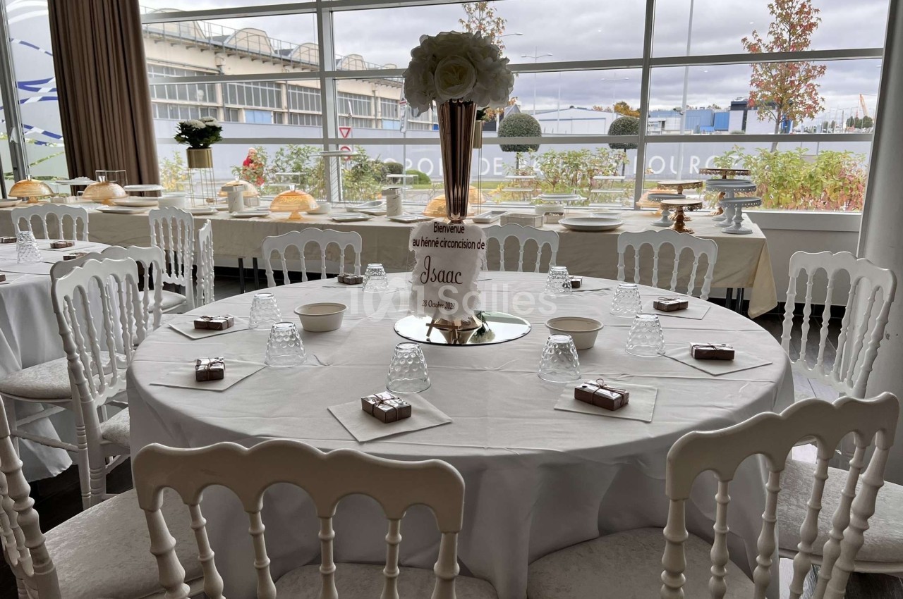 Table de réception décorée avec nappes blanches, chaises assorties, centre de table floral et vaisselle disposée.