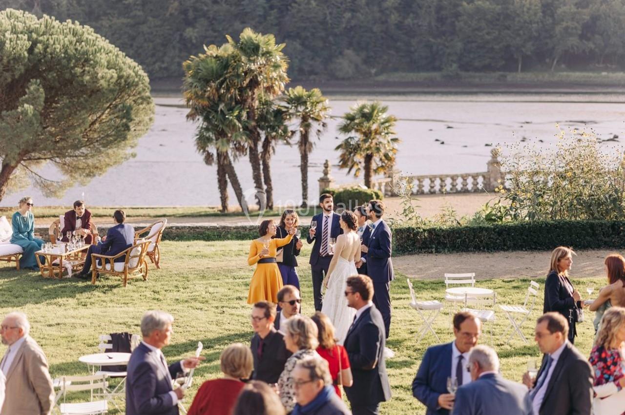 Groupe de personnes discutant dans un jardin près d'un plan d'eau, entouré de verdure et de mobilier de plein air.
