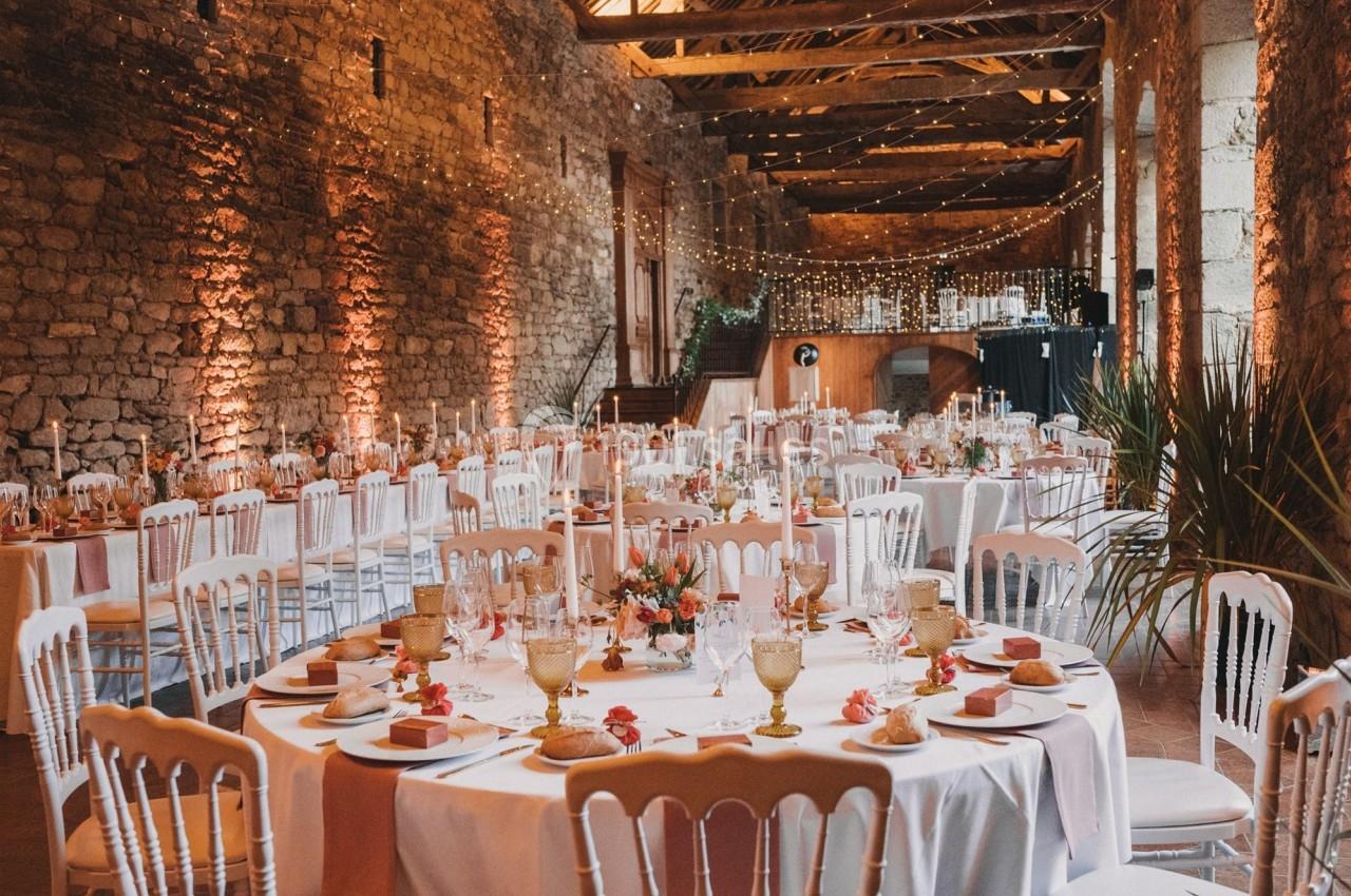 Salle de réception en pierre avec tables décorées pour un mariage, éclairage chaleureux et guirlandes lumineuses suspendues.