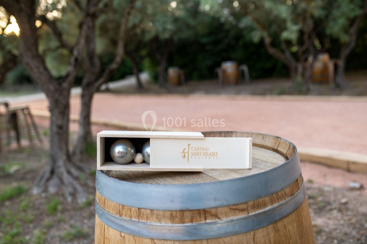 Coffret de boules de pétanque posé sur un tonneau en bois, dans un cadre extérieur avec des oliviers.