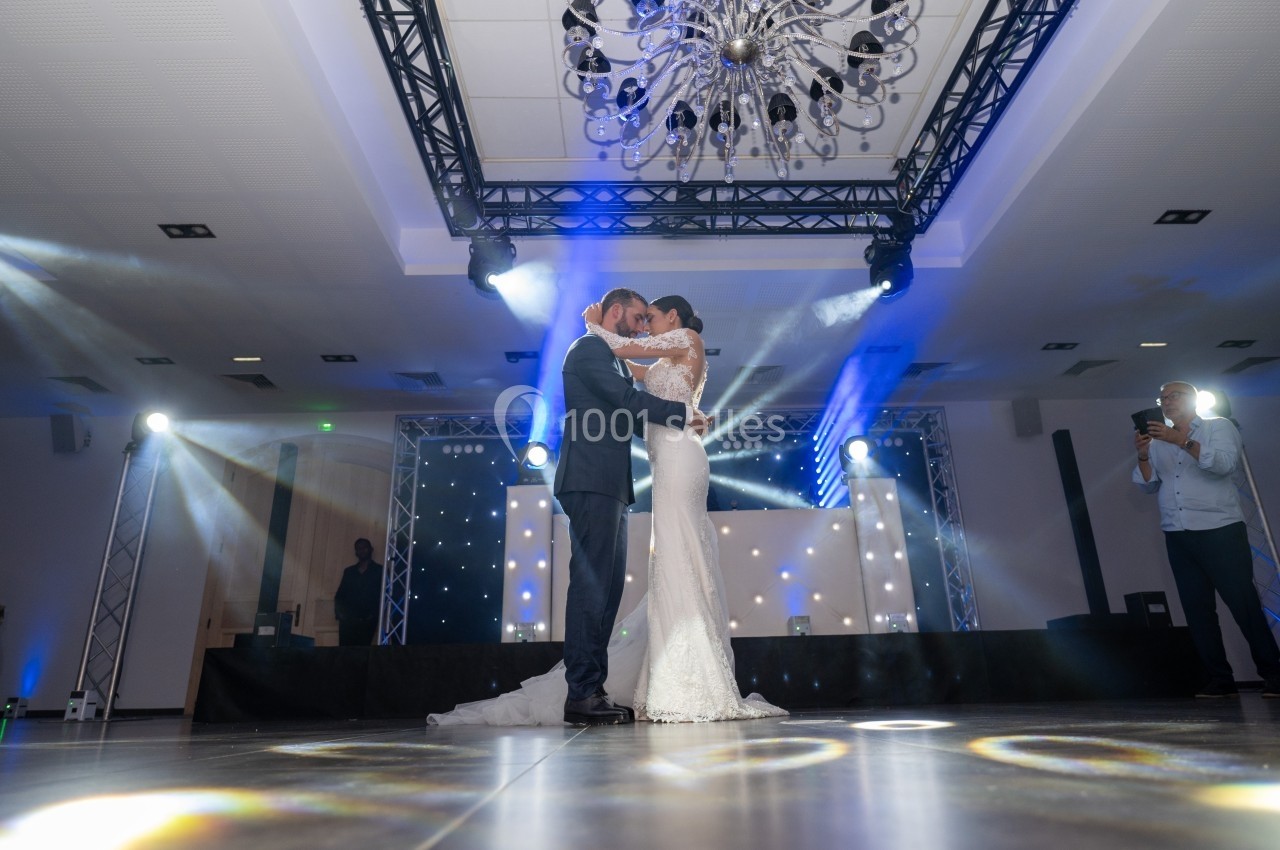 Un couple danse sous un éclairage de fête dans une salle décorée avec un lustre et des projecteurs lumineux.