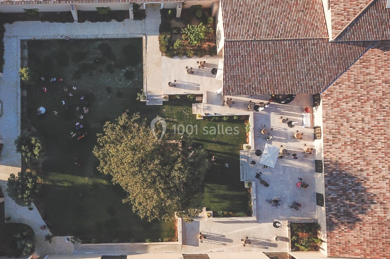 Vue aérienne d'une cour intérieure avec pelouse, arbres, allées pavées et plusieurs personnes dispersées.