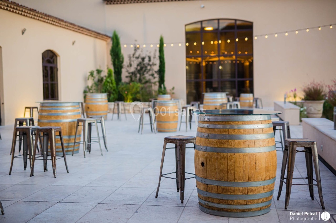 Terrasse aménagée avec des tonneaux en bois servant de tables, entourés de tabourets métalliques, éclairée par des…