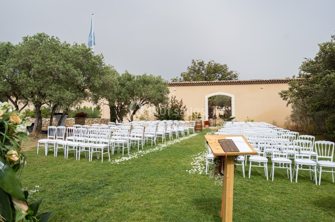 Chaises blanches disposées en rangées sur une pelouse pour une cérémonie en extérieur, avec un pupitre au premier plan.