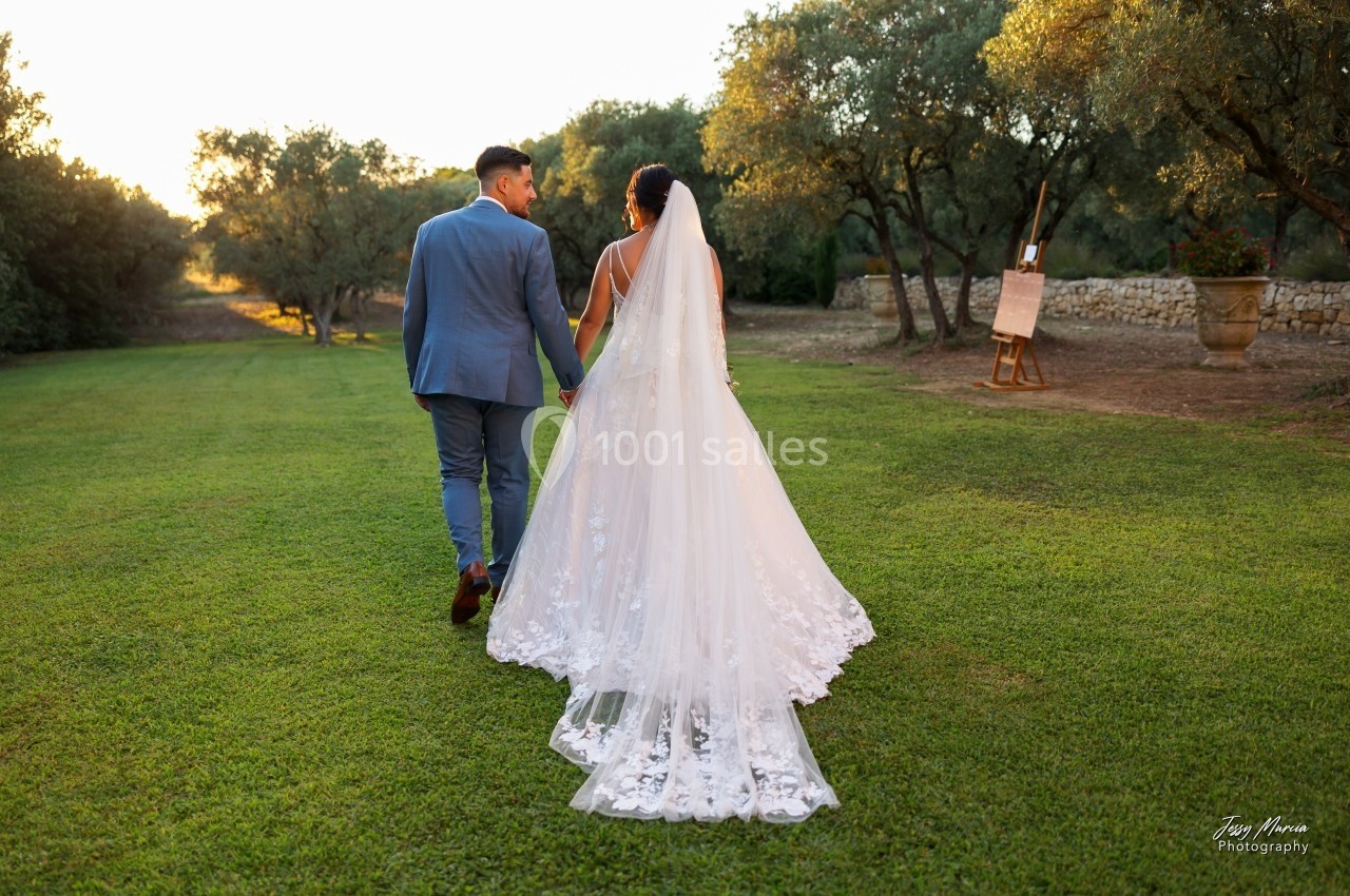 Un couple en tenue de mariage marche main dans la main sur une pelouse au coucher du soleil.