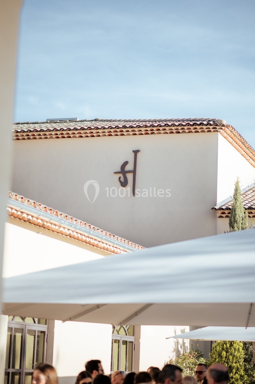 Façade d'un bâtiment avec un toit en tuiles rouges et un logo stylisé, vue sous un ciel dégagé.