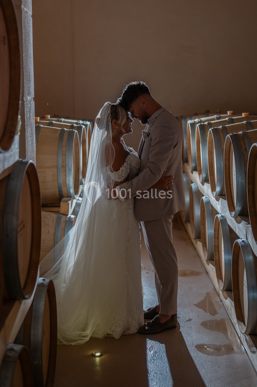 Un couple de mariés s'enlace tendrement dans une cave à vin éclairée par une lumière douce.