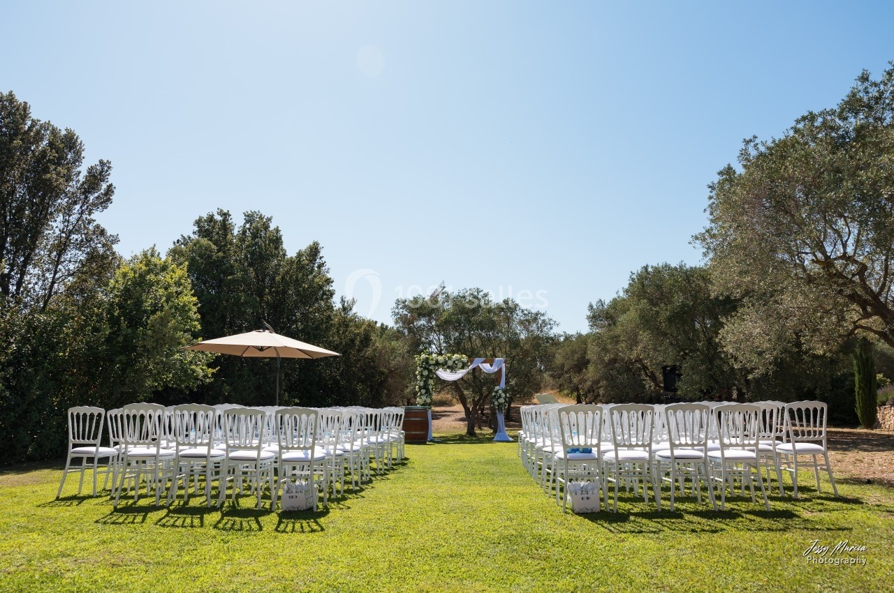 Chaises blanches disposées en rangées sur une pelouse, face à une arche décorée, sous un ciel dégagé.