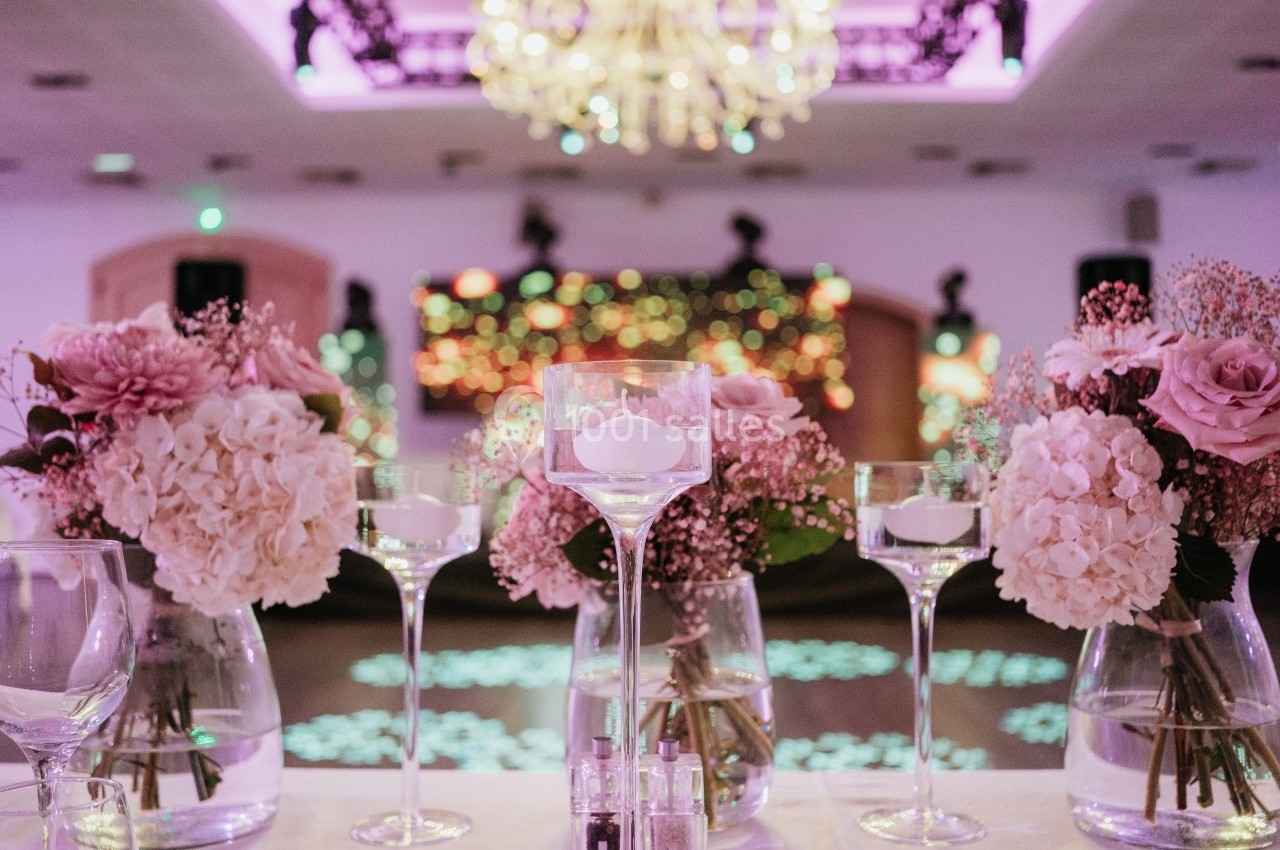 Bougies flottantes et bouquets de fleurs roses décorent une table dans une salle éclairée par des lumières tamisées.