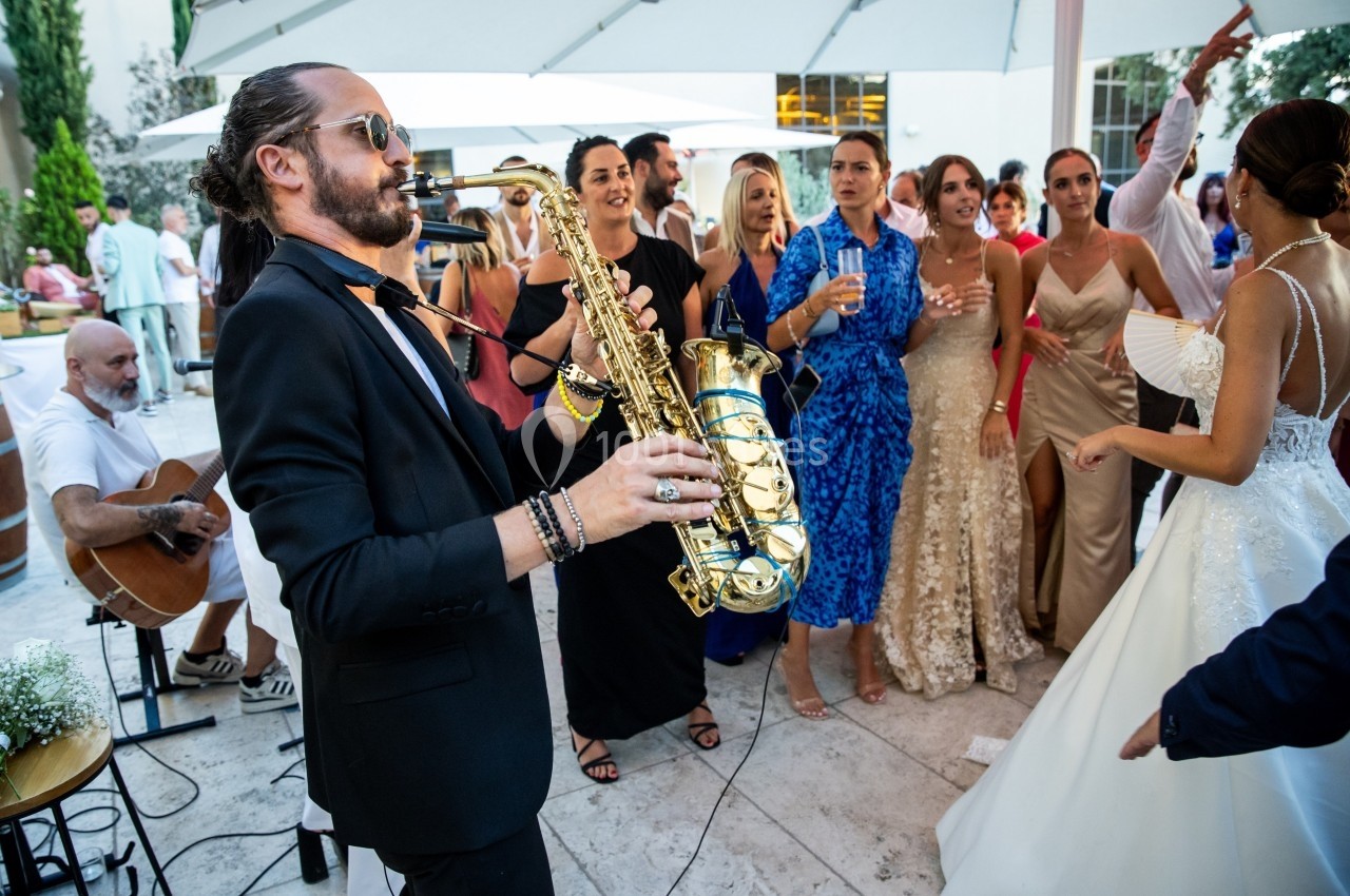Un musicien joue du saxophone lors d'une réception en plein air, entouré d'invités élégamment vêtus.