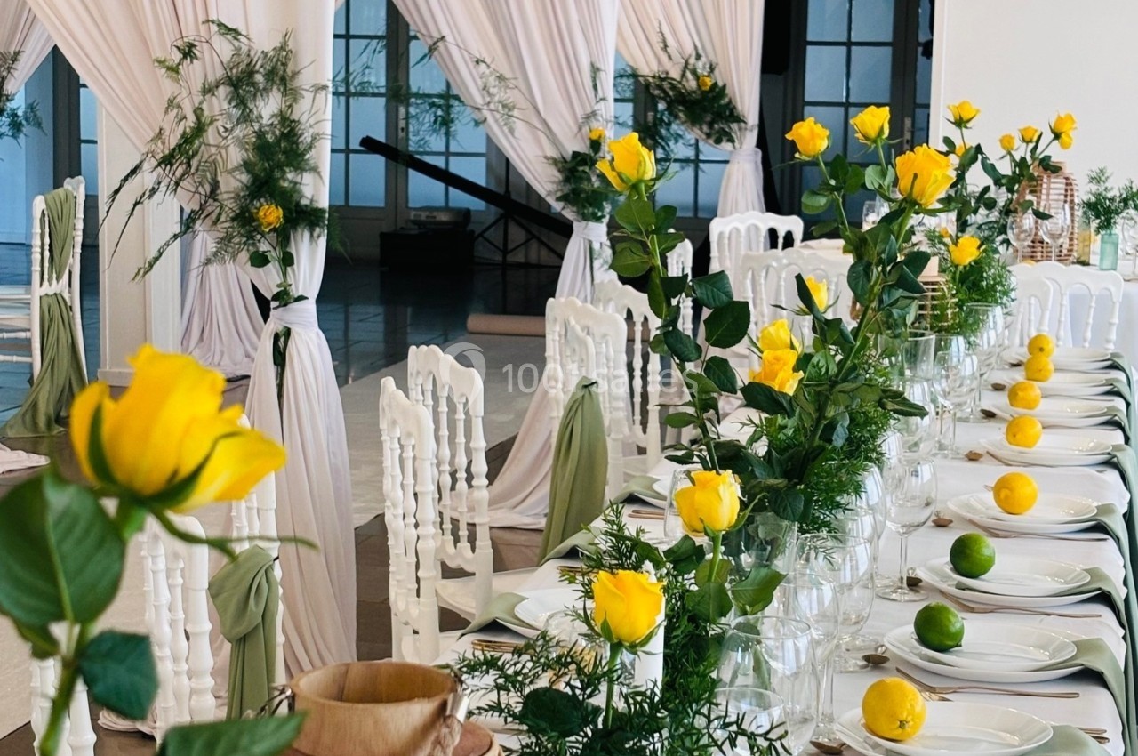 Table décorée avec des roses jaunes, des citrons et des limes, entourée de chaises blanches et de rideaux blancs élégants.