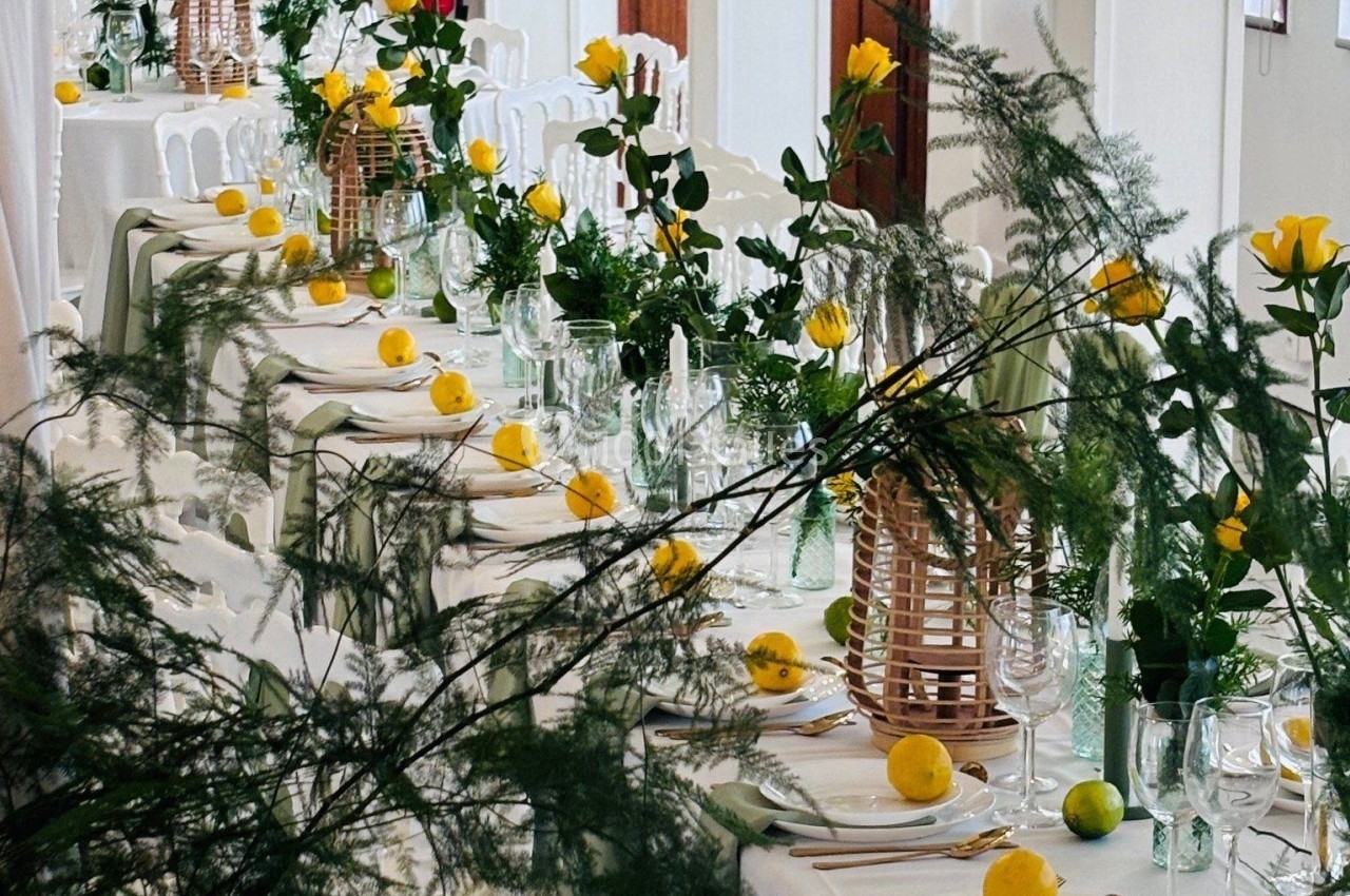 Tables décorées avec des roses jaunes, des citrons et des lanternes en bois dans une salle lumineuse.