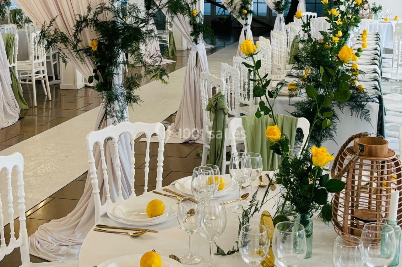 Salle de réception décorée avec des tables dressées, des roses jaunes et des nappes blanches, ambiance élégante et lumineuse.