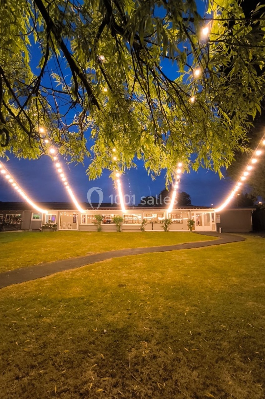 Guirlandes lumineuses suspendues au-dessus d'une pelouse devant un bâtiment éclairé, au crépuscule.