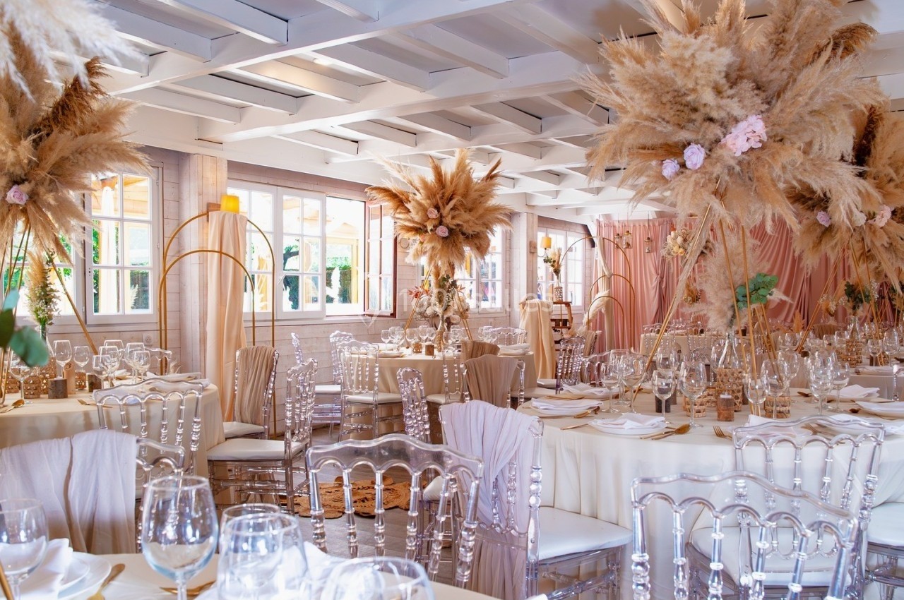 Salle de réception décorée avec des tables élégantes, des chaises transparentes et des compositions florales séchées…