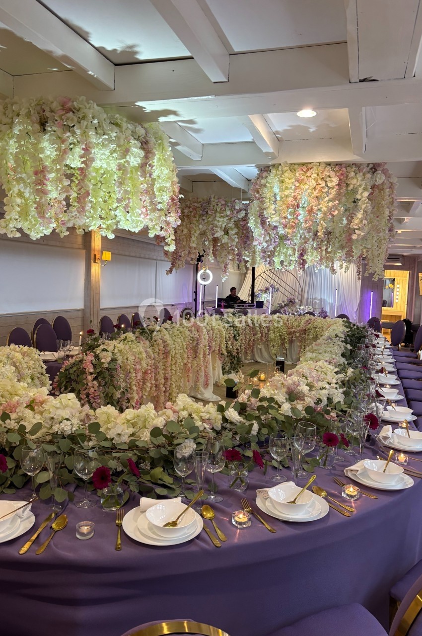 Salle de réception décorée avec des tables violettes, des fleurs suspendues et des arrangements floraux élégants.