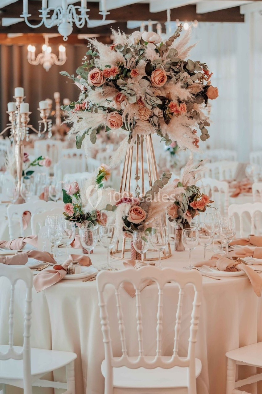 Salle de réception décorée avec des tables rondes, nappes blanches, chaises élégantes et centres de table fleuris.