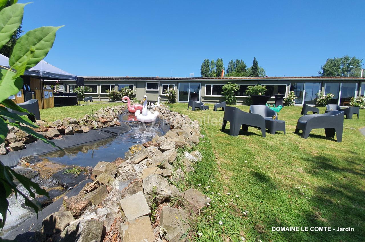 Petit bassin avec des flamants roses décoratifs entouré de chaises et tables dans un jardin verdoyant.