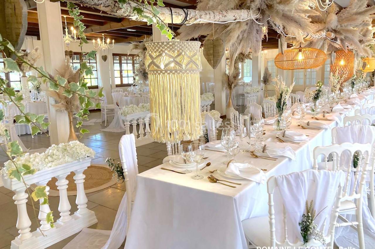 Salle de réception décorée avec des tables dressées, des chaises blanches et des ornements suspendus en fibres naturelles.
