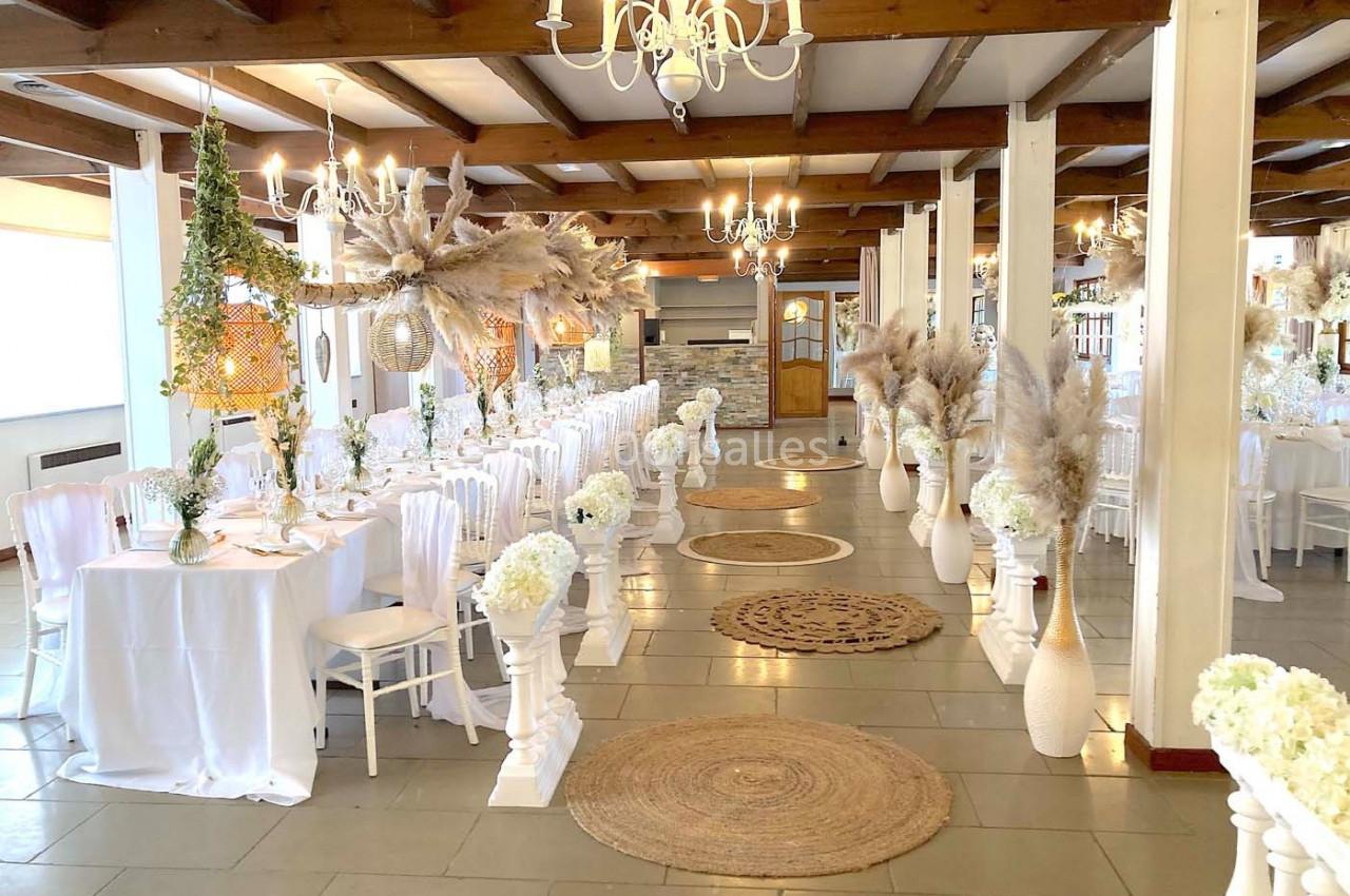 Salle de réception décorée avec des tables alignées, des chaises blanches et des compositions florales élégantes.