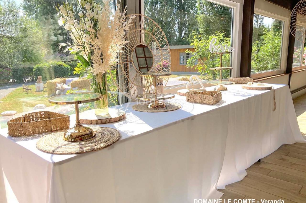 Table décorée avec des éléments en rotin, miroirs et fleurs séchées, placée dans une véranda lumineuse avec vue sur un…