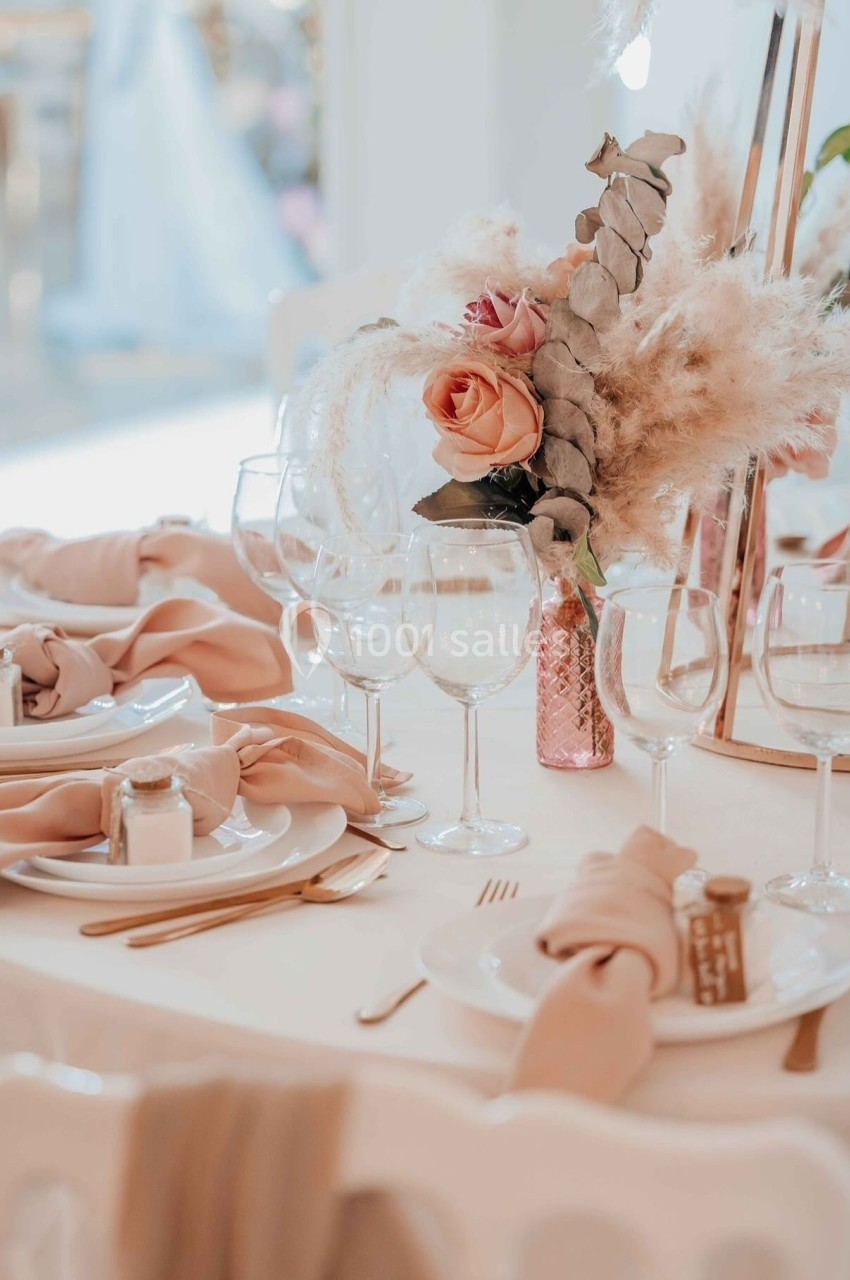 Table élégamment dressée avec vaisselle blanche, serviettes beige rosé et centre de table floral avec pampas et roses.