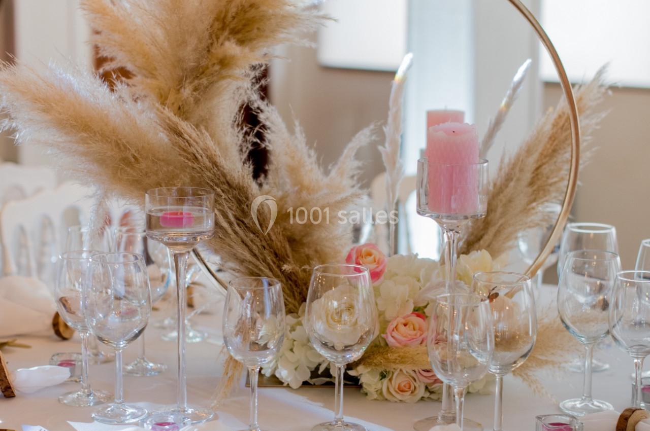 Table décorée pour un événement avec des pampas, des roses, un miroir rond, des bougies roses et des couverts dorés.