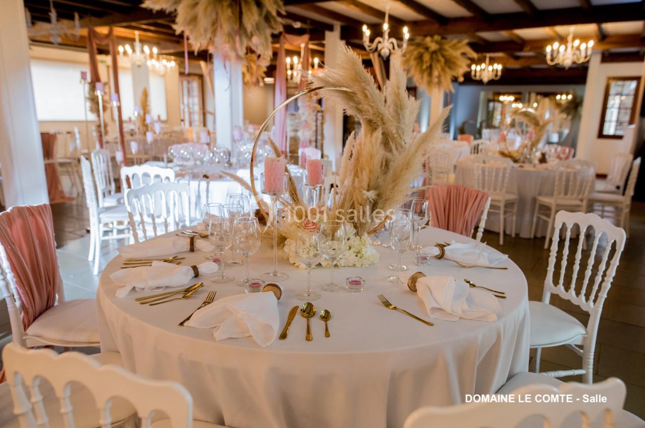Table ronde élégamment dressée avec des couverts dorés, des serviettes blanches et une décoration florale centrale.