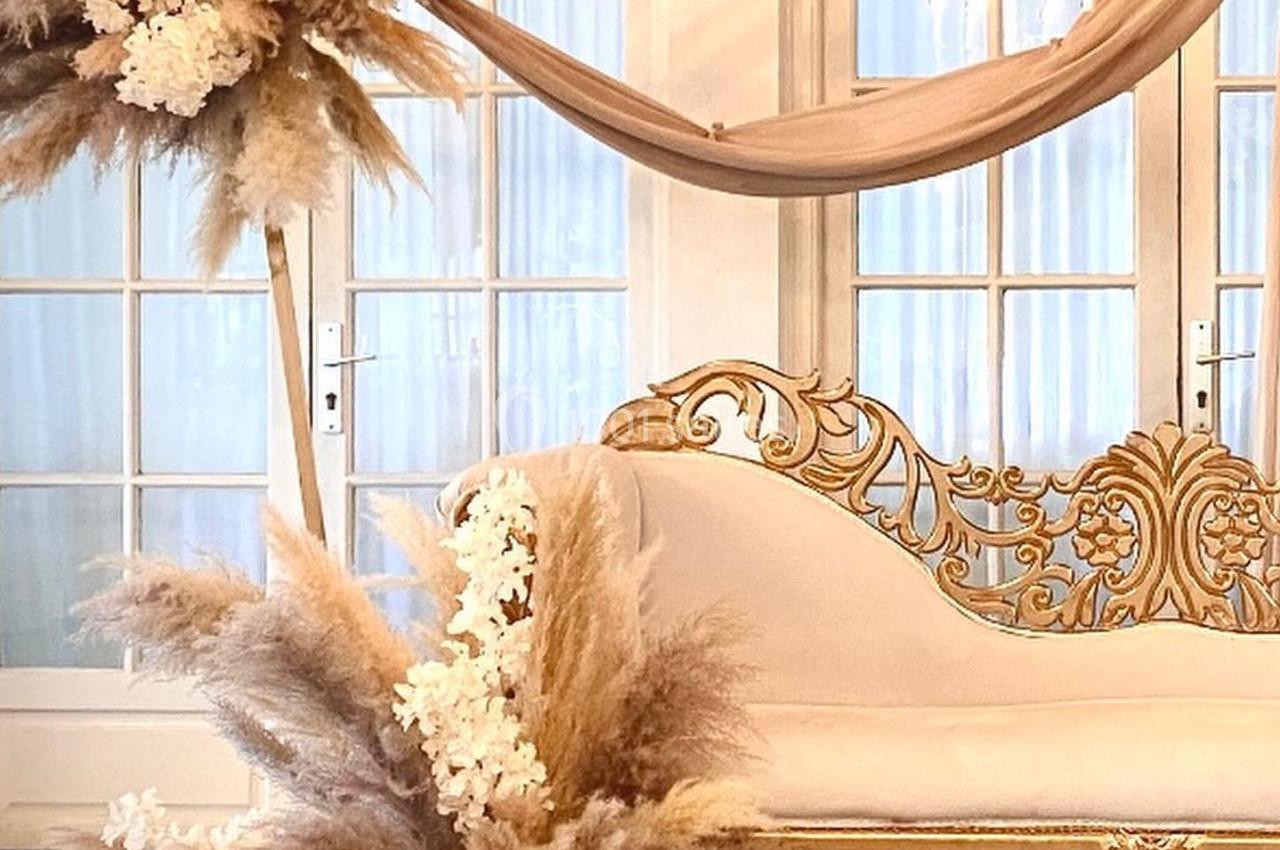 Décoration élégante avec canapé doré, drapé beige et compositions florales de pampas et fleurs blanches.