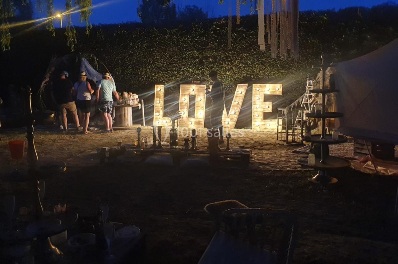 Décoration lumineuse formant le mot ’LOVE’ dans un espace extérieur en soirée, avec des stands et des personnes autour.