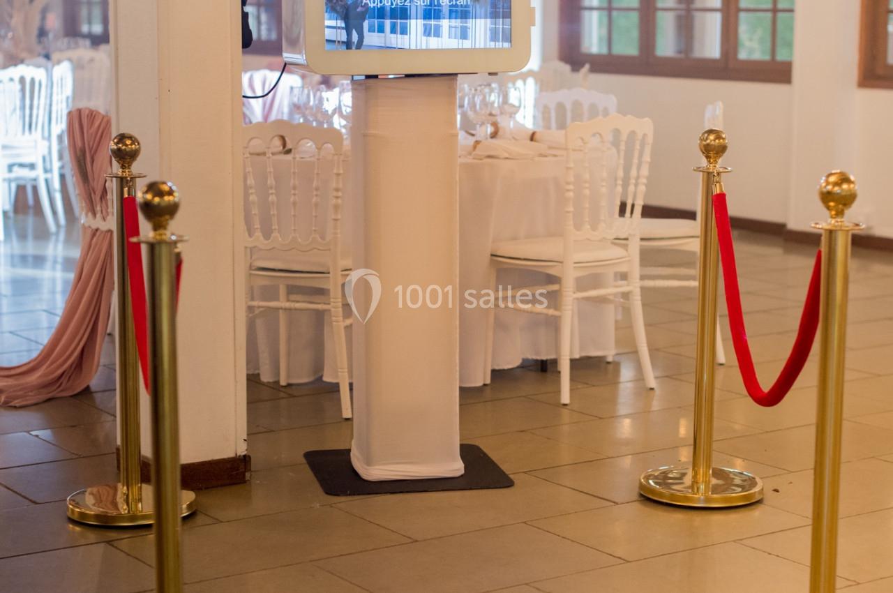 Borne photo interactive installée dans une salle de réception élégante avec chaises blanches et décorations raffinées.