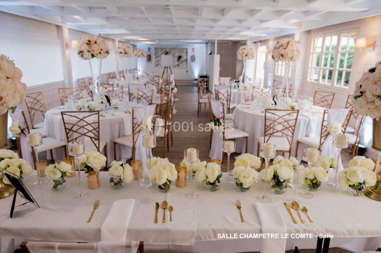 Salle de réception décorée avec des tables rondes, nappes blanches, chaises dorées et arrangements floraux élégants.