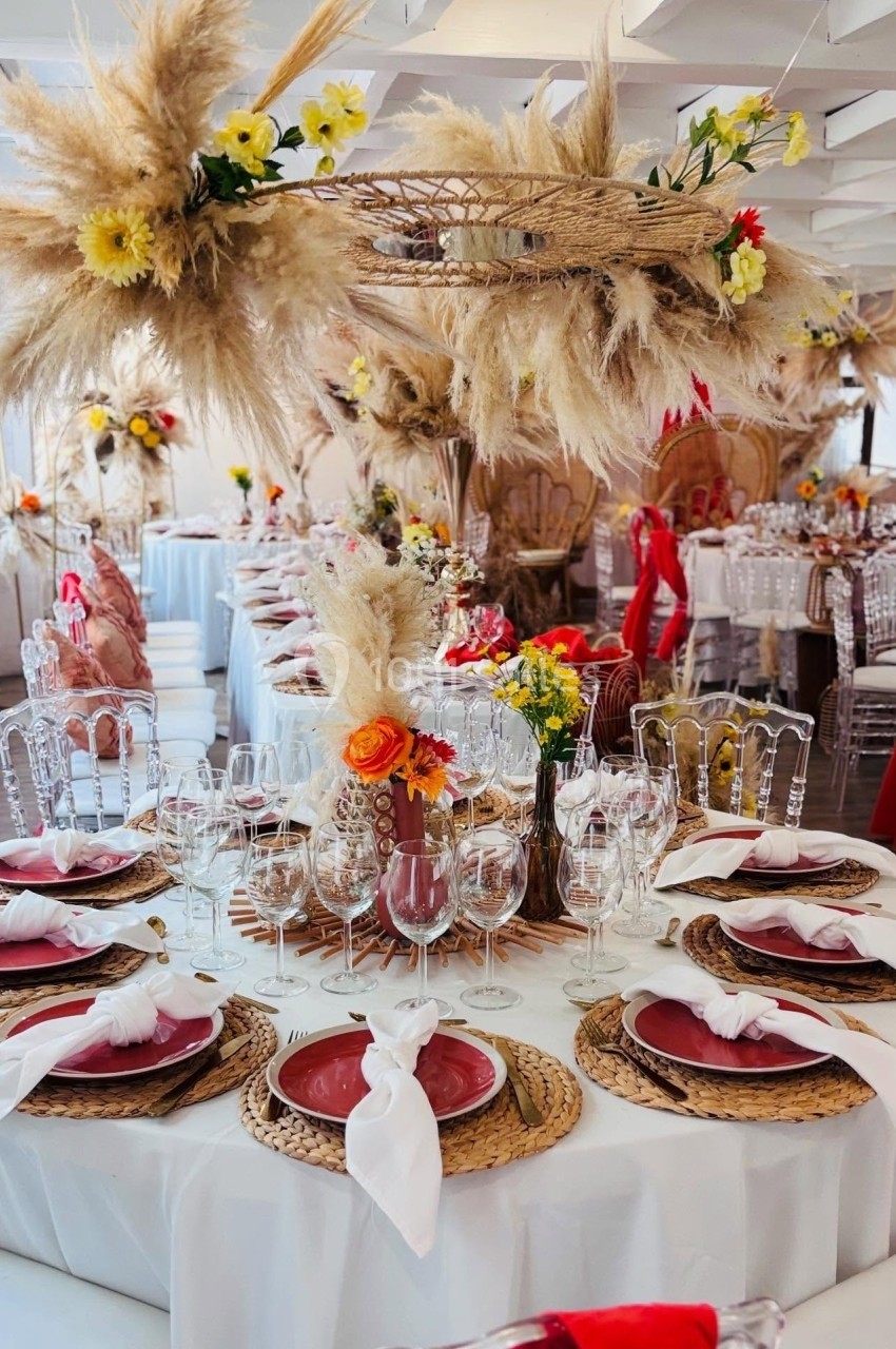 Table décorée pour un événement avec des assiettes rouges, des serviettes blanches et des arrangements de fleurs et pampas.