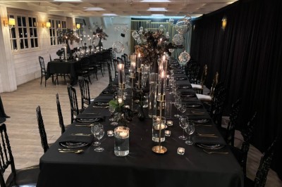 Salle de réception élégante avec décoration noire et dorée, tables dressées et bougies allumées.