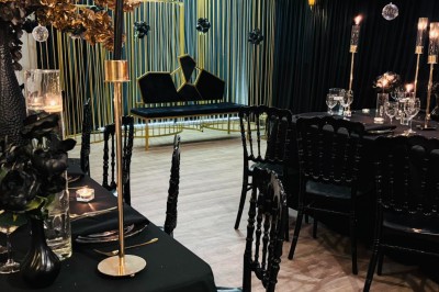 Salle de réception élégante avec décoration noire et dorée, tables dressées et bougies allumées.