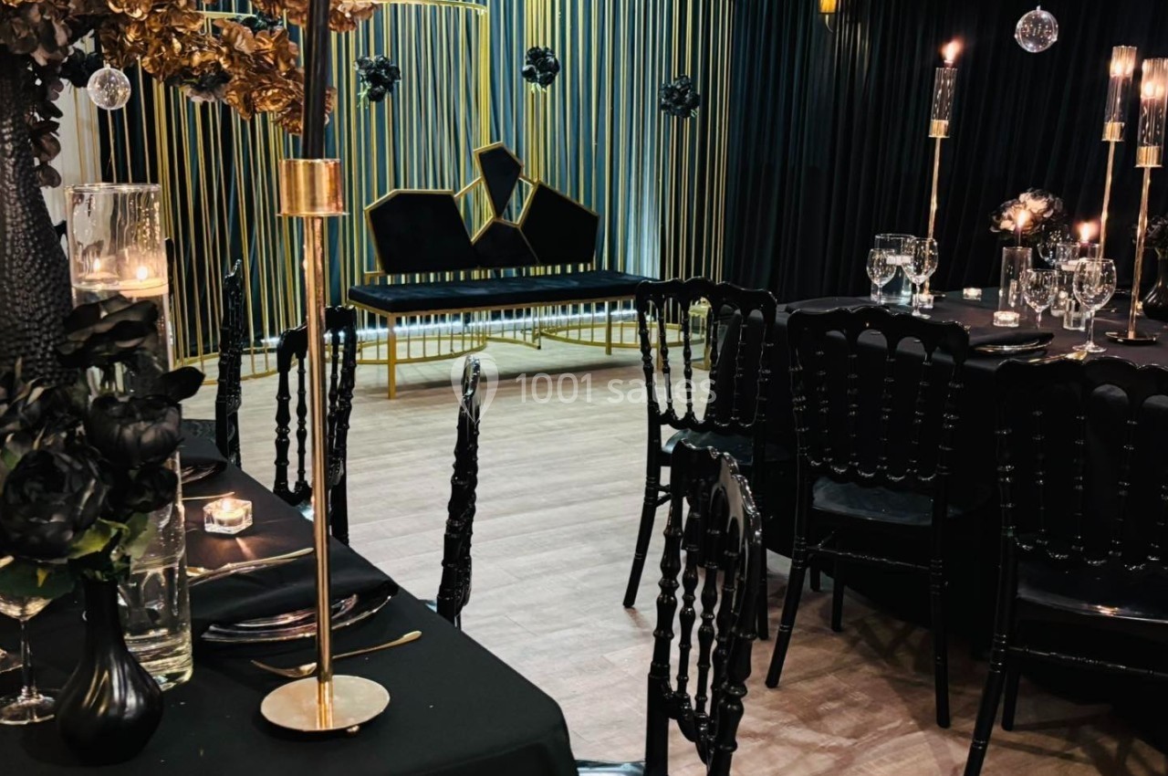 Salle de réception élégante avec décoration noire et dorée, tables dressées et bougies allumées.