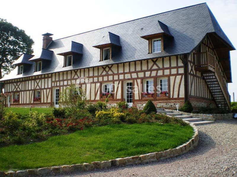 Maison à colombages avec toit en ardoise, entourée d'un jardin fleuri et d'une allée en gravier.